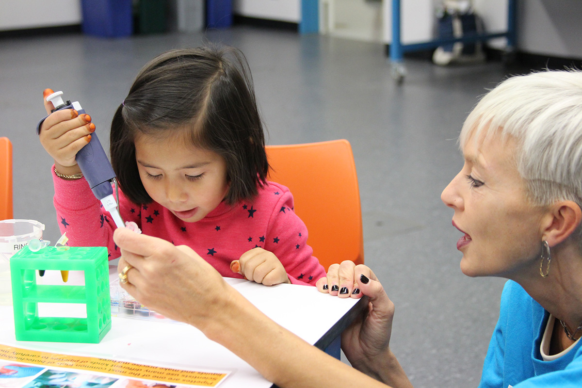 A Lawrence educator teaches a child how to use a pipette