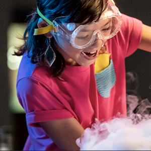 A young person wearing safety goggles pours liquid during a science demonstration