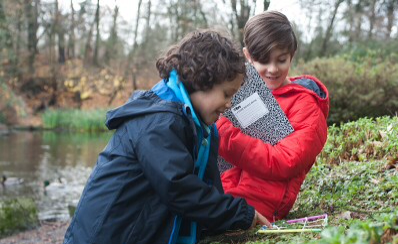 Two young people investigating nature outdoors near a lake.