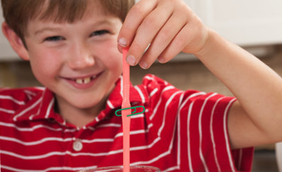A child holding up a straw and a paperclip to simulate clogged arteries