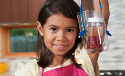 A child holding up a jar with red liquid in a plastic bottle to represent blood in a science experiment