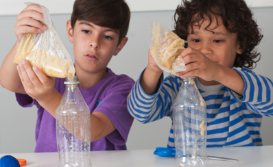 Two children pouring a mashed banana into plastic bottles for their science experiment