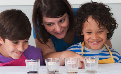 An adult and two children with four glass of different substances they are testing in their science experiment what does spit do