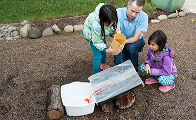 Two children and an adult pouring lake water into a bucket for a science experiment.