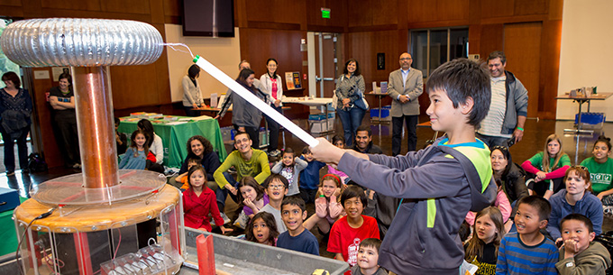 A young scientist experiments with the Hall's Tesla Coil in front of a crowd.
