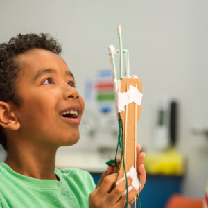 A smiling student holds up the science project he has constructed.