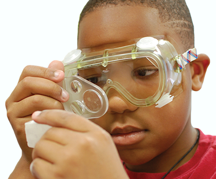 A child is wearing safety glasses and looking through a magnifying object