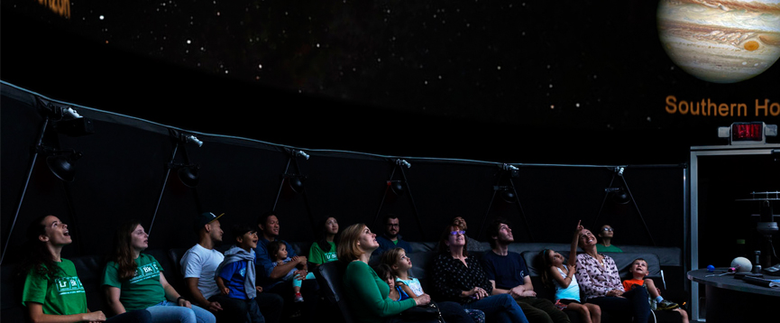 A group of people sitting in the planetarium and looking up at the stars