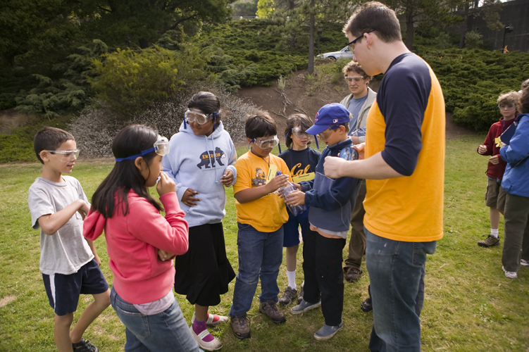 A group of students is outdoors with their teacher while they participate in a science activity