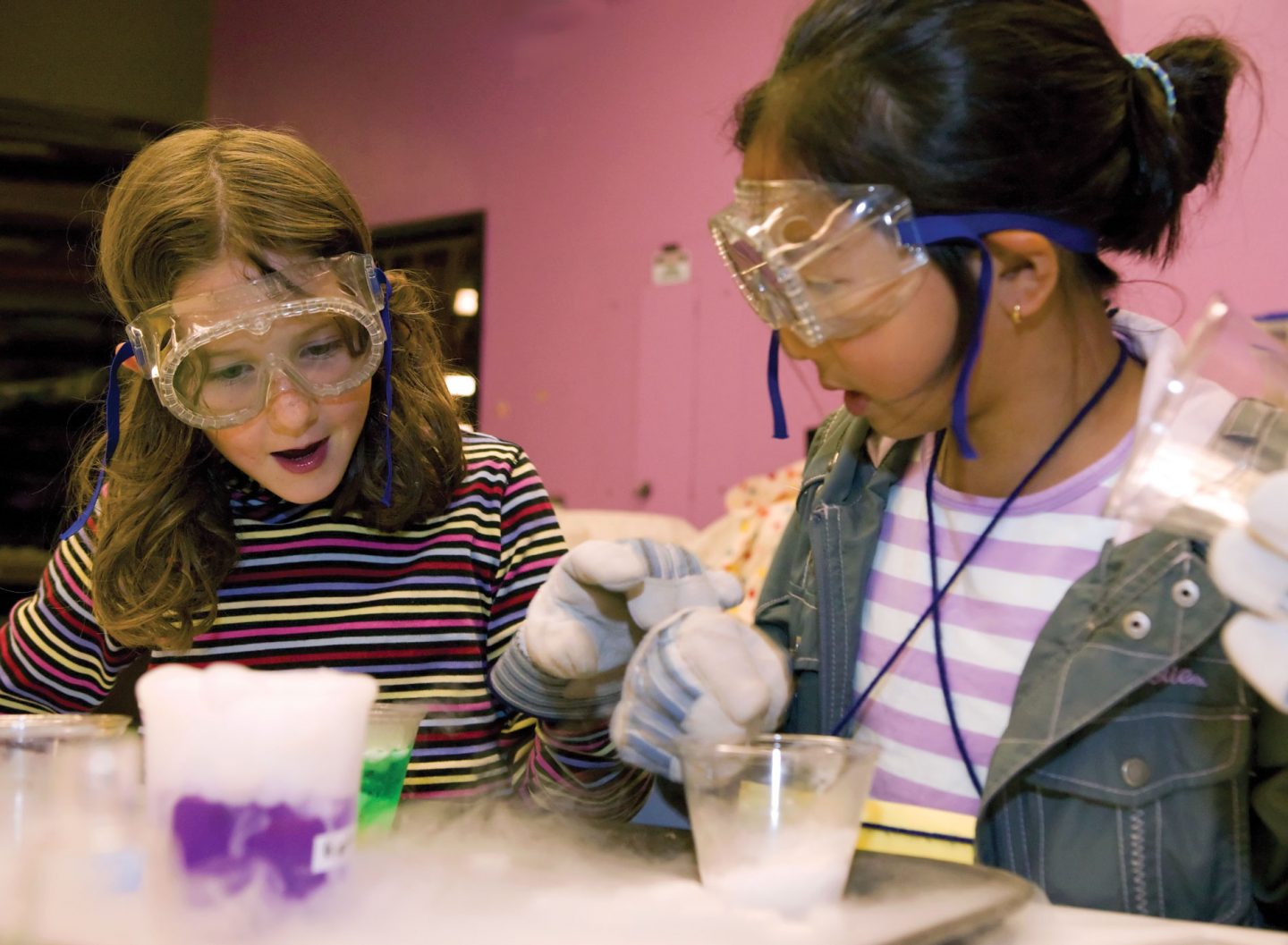 Two young people wearing safety glasses and gloves are working on a science experiment examining foaming liquid