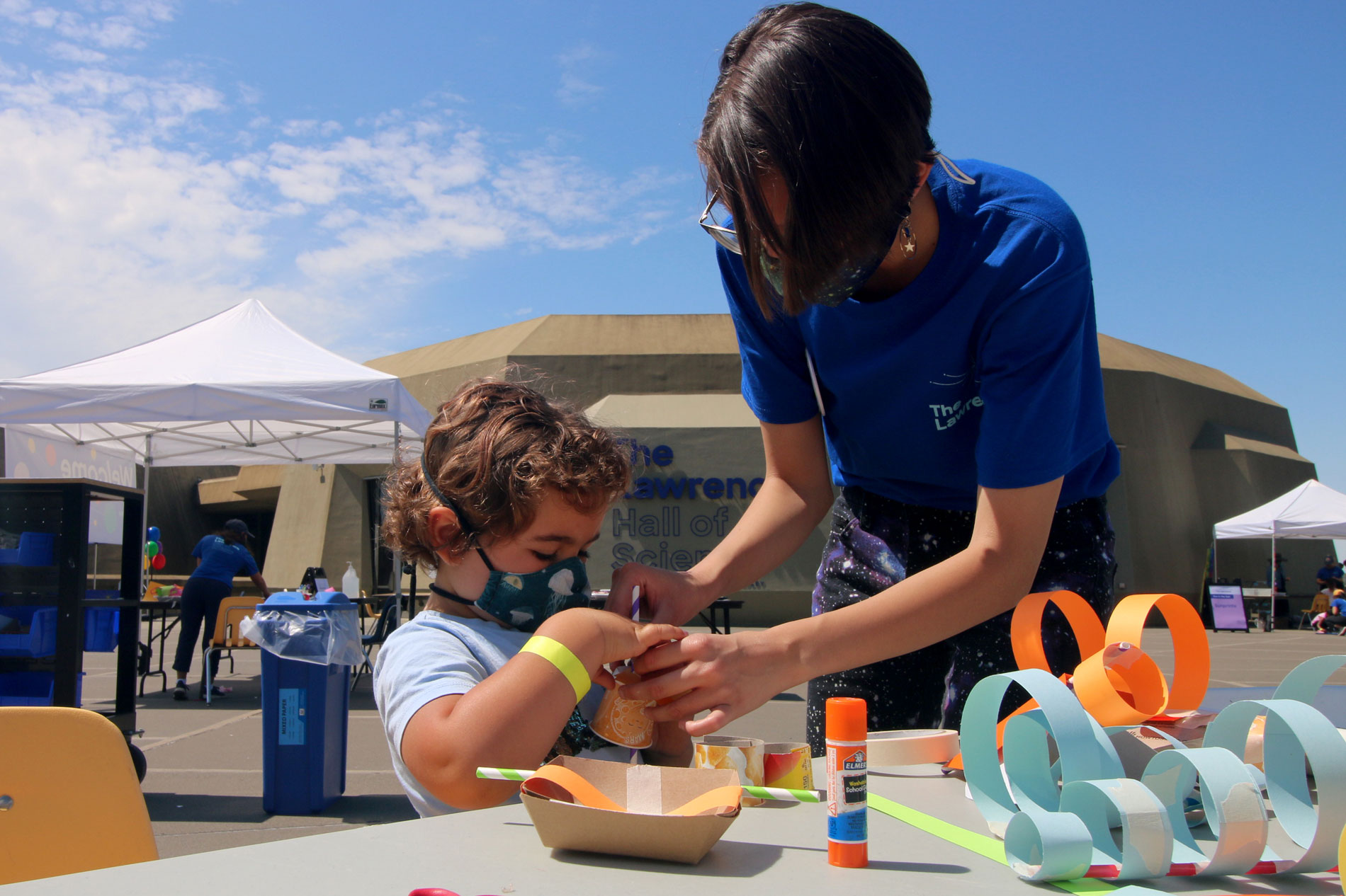 A staff member helping a child with a paper sculpture during Summer Fundays