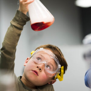 A young person holding up a science beaker and examining the red liquid