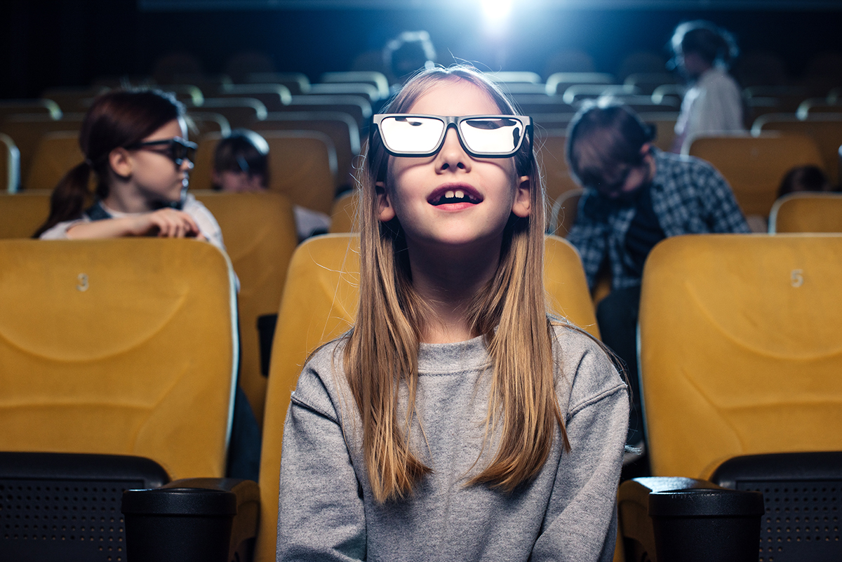A girl wearing 3D glasses watching a movie in a theater