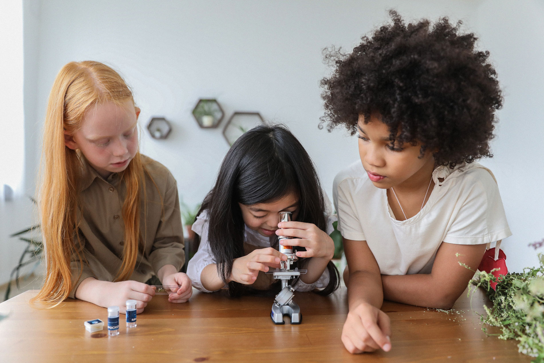 A child looking through a microscope with two children looking on