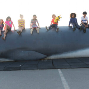 A row of children sitting on top of Pheena the Fin Whale