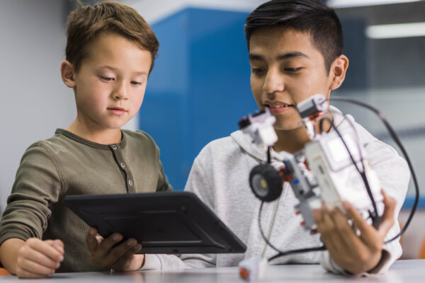 Younger child holding tablet while older student holds robotic car.