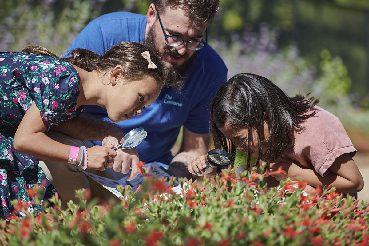 Two girls and a staff member investigate flowers in the Outdoor Nature Lab