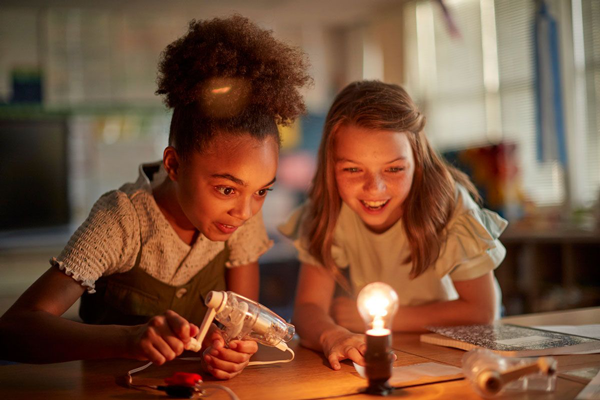 Two students light up a light bulb during a science project.