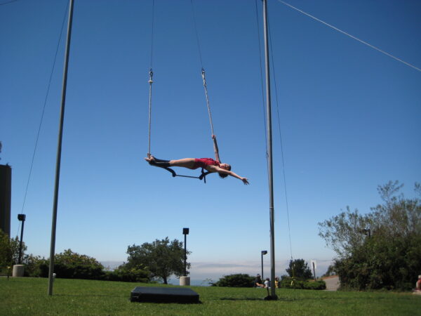 A young trapeze performer suspended in the air with a view of the San Francisco Bay in the background