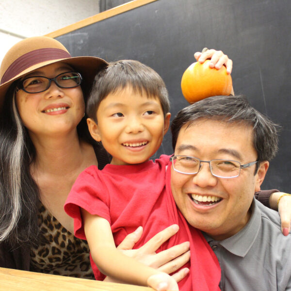 Two parents and their child holding a pumpkin and smiling at the camera