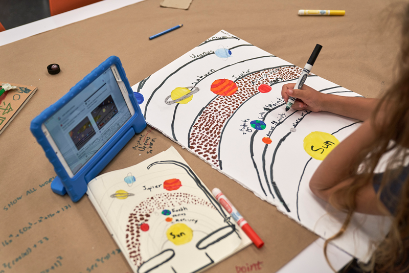 A camper is drawing the solar system and orbit of the planets during the Surviving on Mars Summer Camp.
