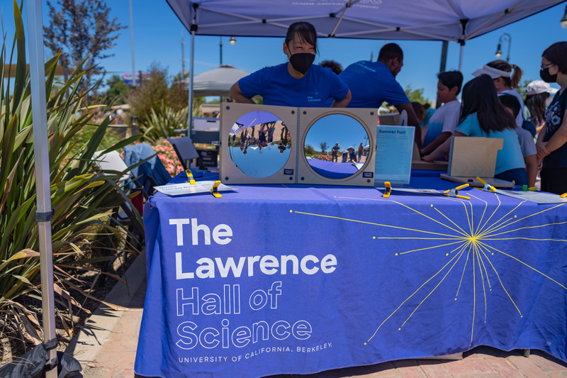 A Lawrence On-The-Go staff member is at The Lawrence's booth with a science activity during a community event