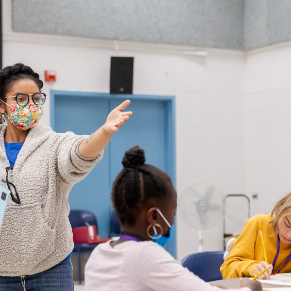 A summer camp educator is facilitating a classroom activity. Two students are seated at a table.