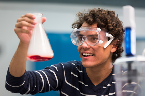 A student is holding up a science beaker and examining the red liquid inside