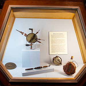 An exhibit display case containing several small early cyclotron models and a panel of text about the devices.