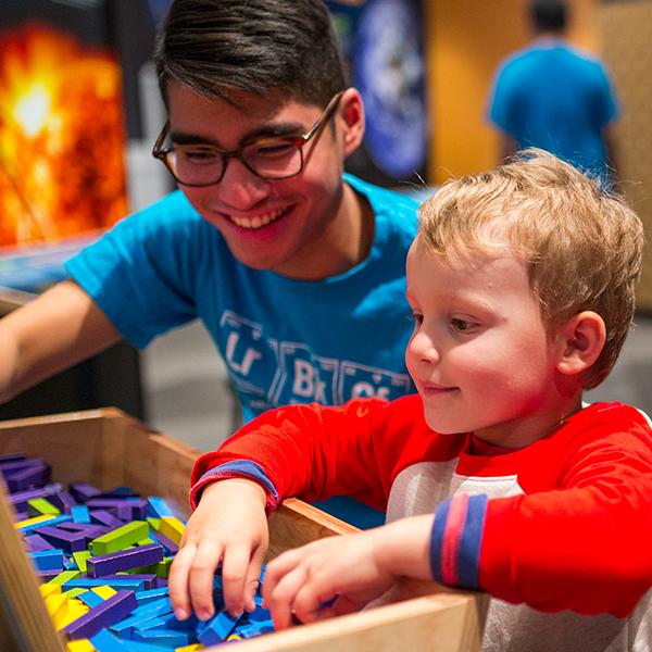 A teen volunteer helps a young child at an exhibit