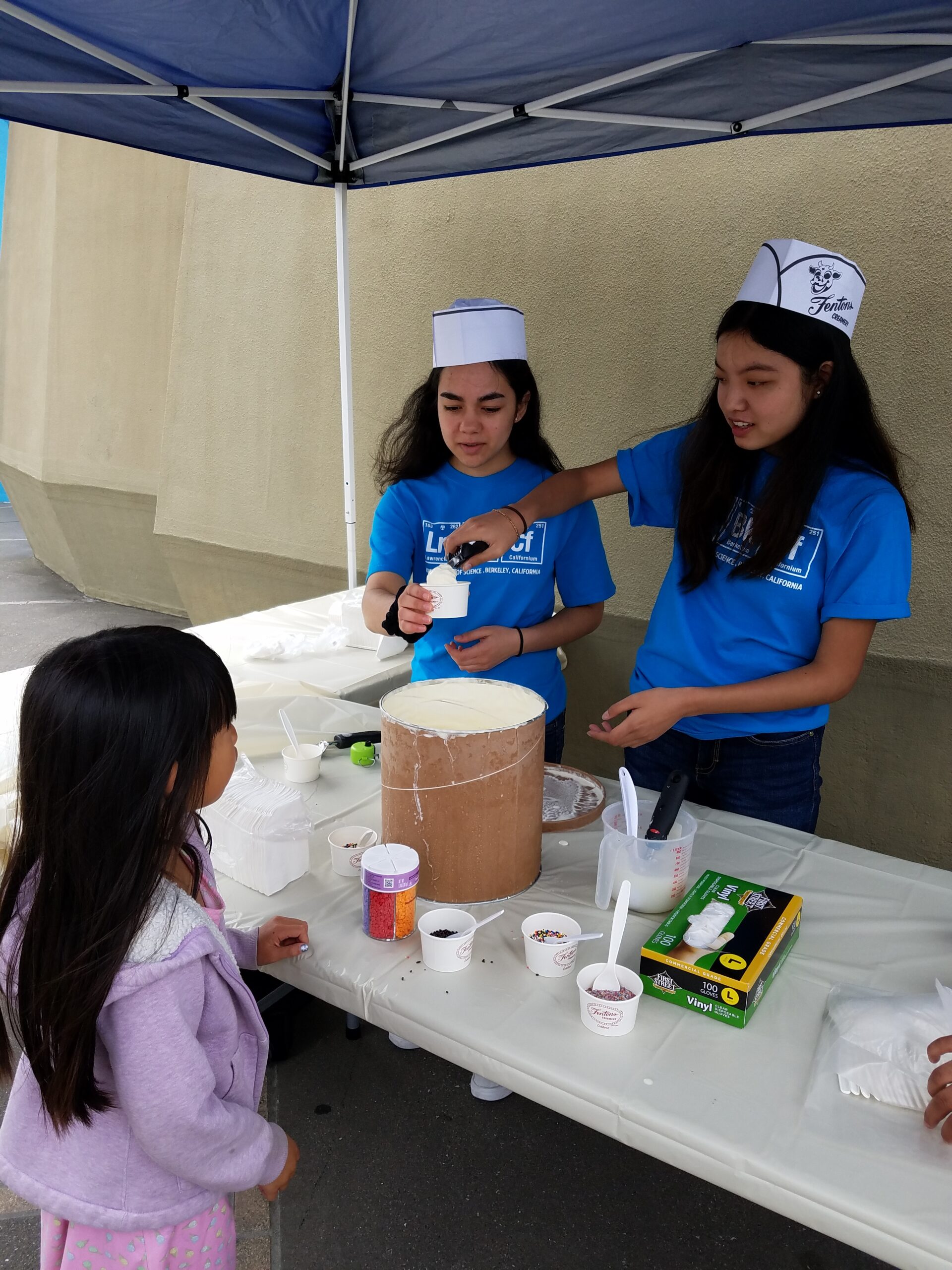 Two Lawrence Hall of Science volunteers serve ice cream to a young visitor