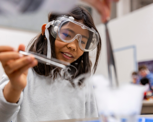 A child wearing safety goggles is conducting a science experiment using dry ice.