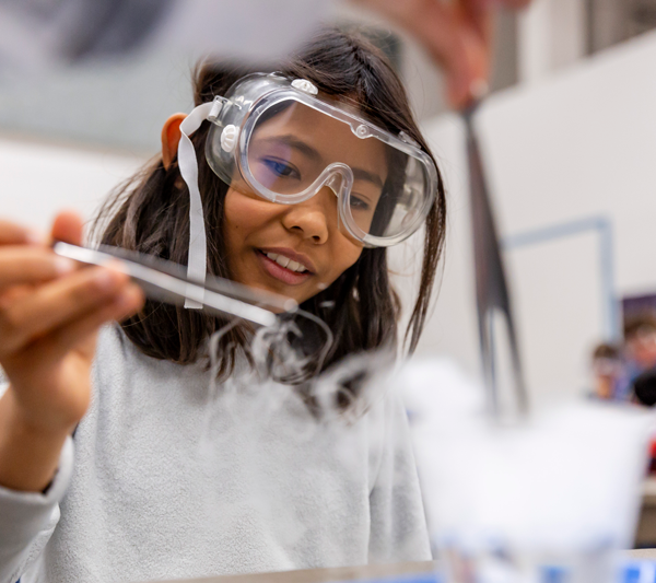 A child wearing safety goggles is conducting a science experiment using dry ice.