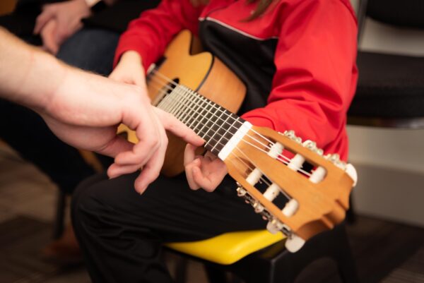 A close up of a child holding a guitar and an adult showing them how to play