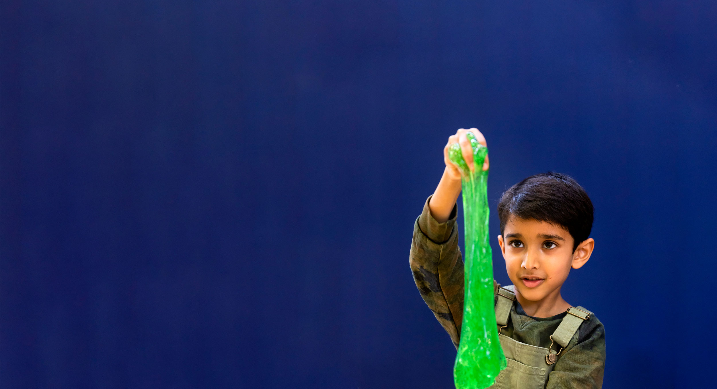 A child is holding up and examining green slime during a science activity
