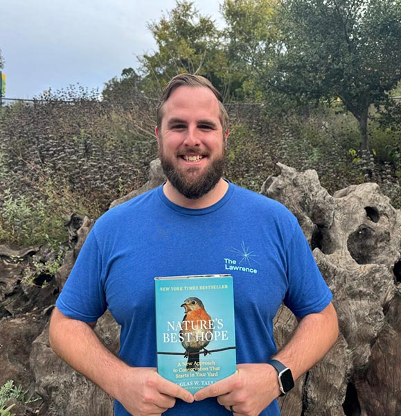 Outdoor Nature Lab Program Lead Chris Ziska holds up the book Nature's Best Hope by Douglas W. Tallamy, his staff pick favorite from the Lawrence Discovery Store.