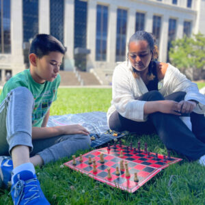 A mentor is mentoring a teen while they play a chess game together on campus