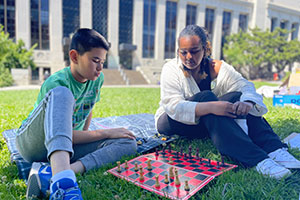 A mentor is mentoring a teen while they play a chess game together on campus