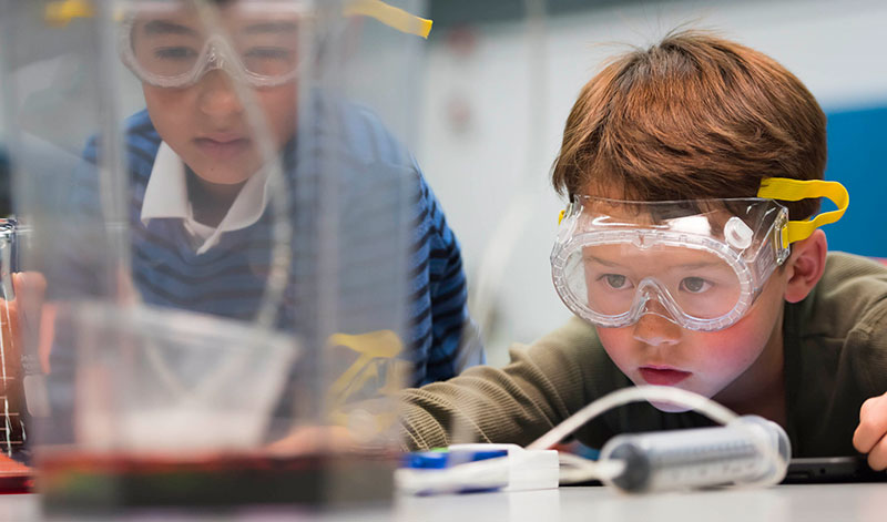 Two students wear safety glasses and participate in a science activity