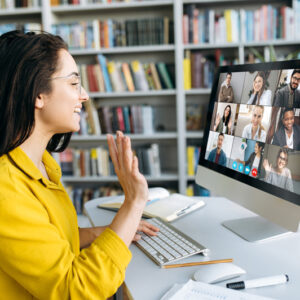 A woman waves at her colleagues during a video call on her laptop