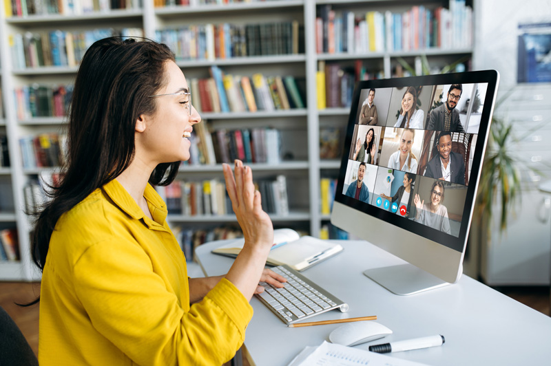 A woman waves at her colleagues during a video call on her laptop