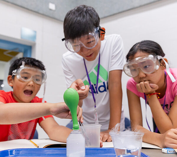 Three youth are conducting a science experiment with dry ice and wearing safety glasses.