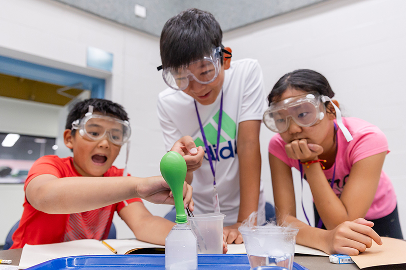 Three youth are conducting a science experiment with dry ice and wearing safety glasses.