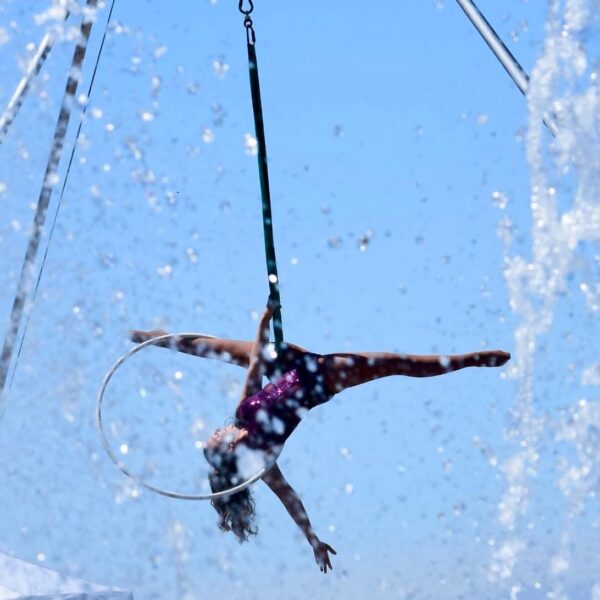 Trapeze artist performing with blurred water fountain water framing the artist