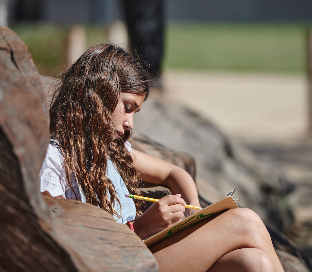 A youth sits outdoors and is writing during a nature journaling activity.
