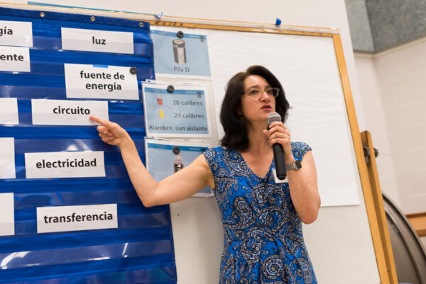 An educator is speaking into a microphone while presenting and pointing to word cards on the classroom wall.