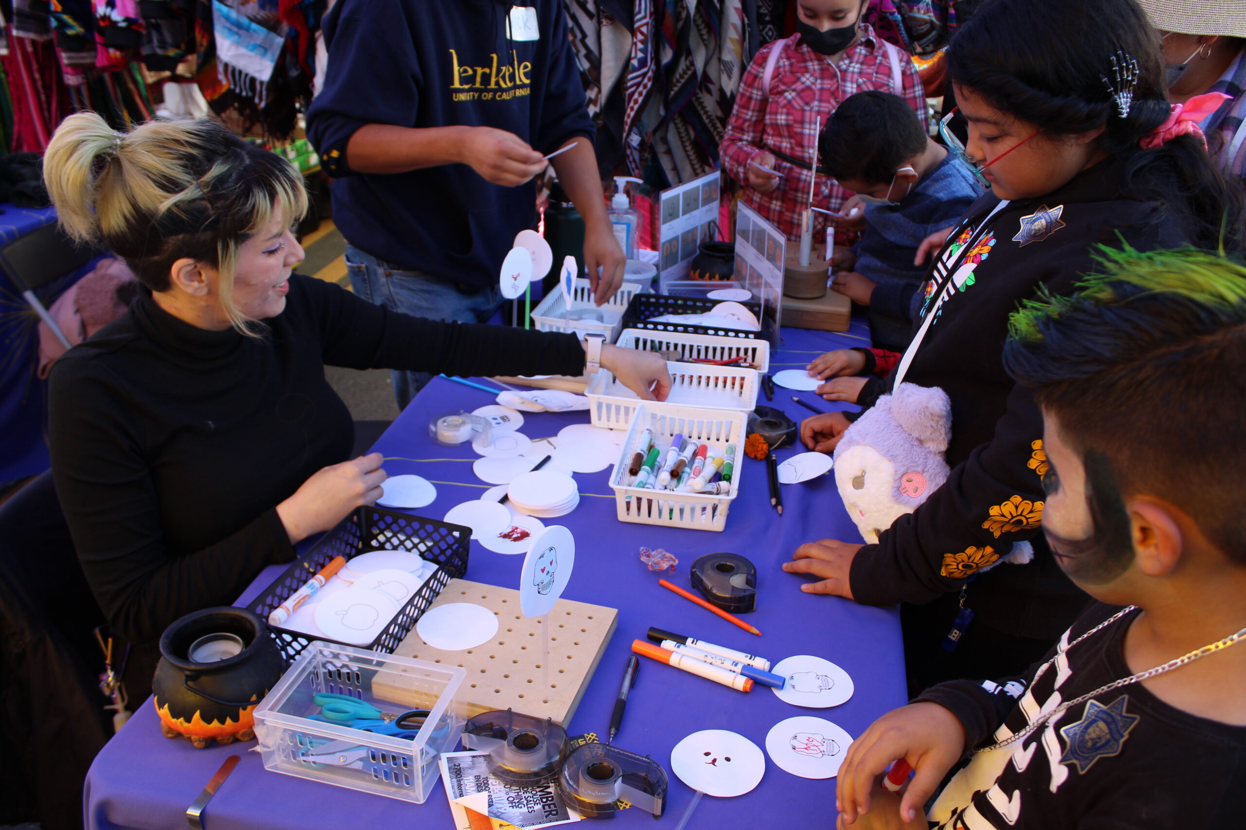 Adults and children participating in a craft activity at a community event, with materials such as paints and brushes on the table.