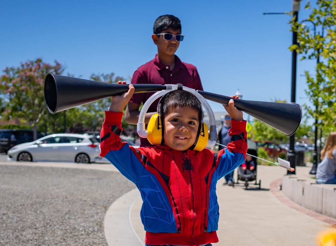 A young child wearing a red jacket and listening to a large black listening device.