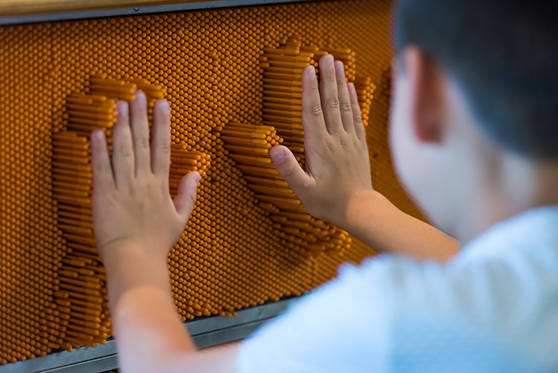 A visitor places their hands on the pin wall in the Young Explorers Area