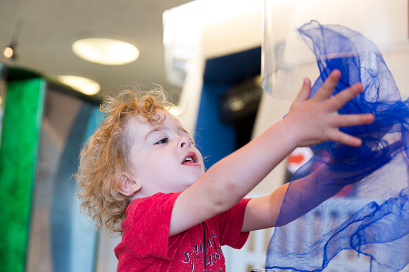 A young visitor launches lightweight fabric into the wind tunnel in the Young Explorers Area